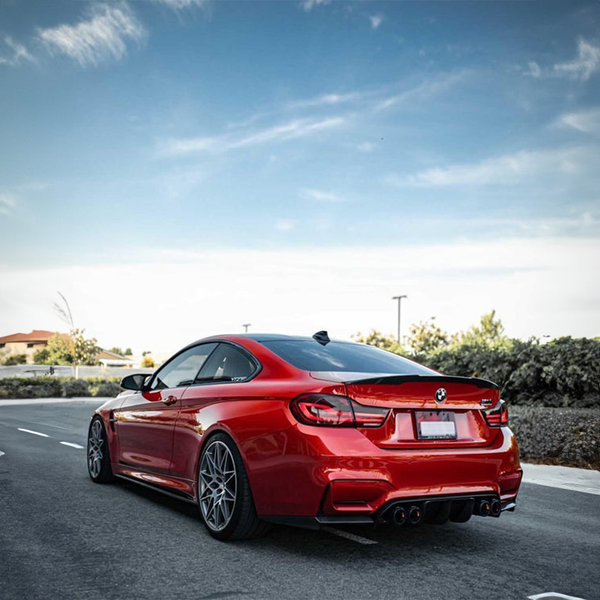 Rear three-quarter view of a red BMW M4 (F82) with a carbon fiber rear spoiler and diffuser, parked on a road under a partly cloudy sky in Australia